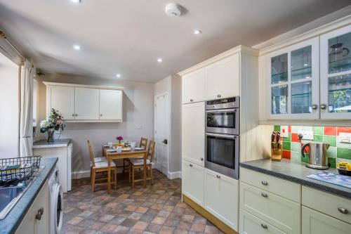 a kitchen with white cabinets and a table with chairs at Clover Cottage in Wyck Rissington