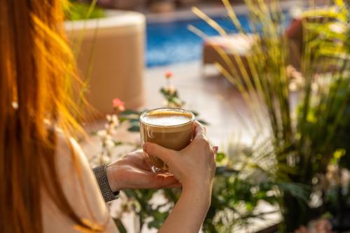 a woman is holding a cup of coffee at Sedra Arjaan by Rotana in Doha