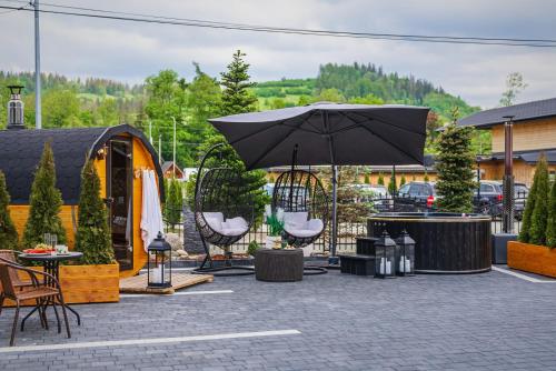 a patio with a black umbrella and chairs and tables at GORSKI RESORT Lux Apartments Jacuzzi & Sauna in Poronin