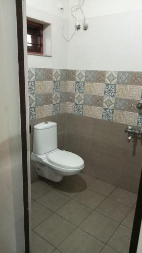 a bathroom with a toilet and a tiled wall at Tejus Home Stay in Alleppey