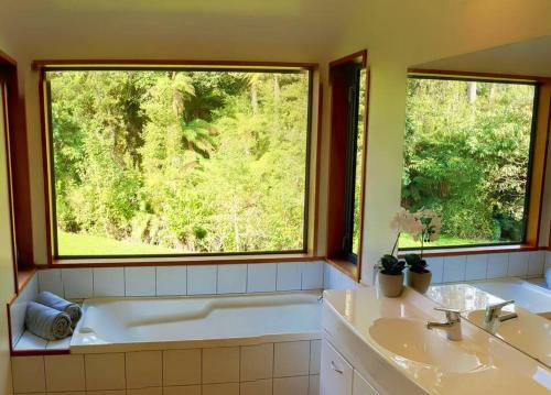 baño con bañera, 2 lavabos y ventana en The Ferns Hideaway en Franz Josef