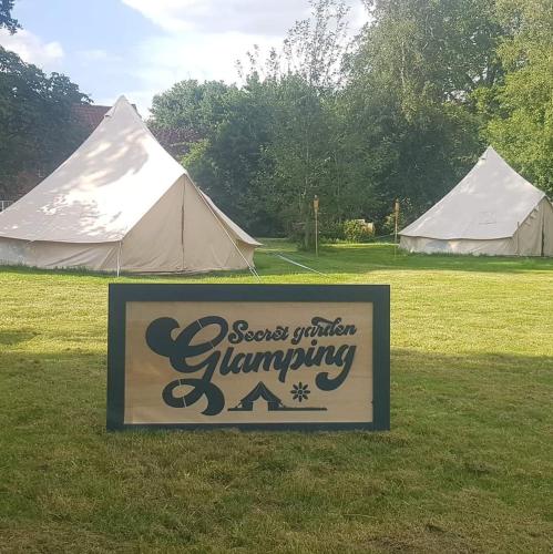 a sign in the grass next to two tents at Bedouin tent Secret garden glamping 