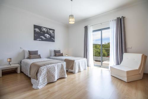 a bedroom with two beds and a chair and a window at Villa Maya by Algarve Holidays in Almancil