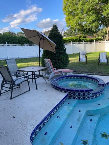 a patio with a table and chairs and an umbrella at Walk to Indian Rocks Beach Exclusive Use of Hot Tub, Pool, BBQ,with Privacy in Largo