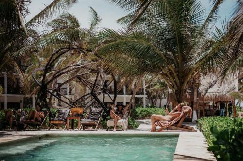 a group of people sitting around a swimming pool with palm trees at Selina Tulum in Tulum