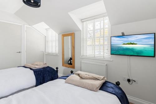 two beds in a bedroom with a tv on the wall at A modern and cosy apartment just yards from Brixham’s bustling harbourside in Brixham