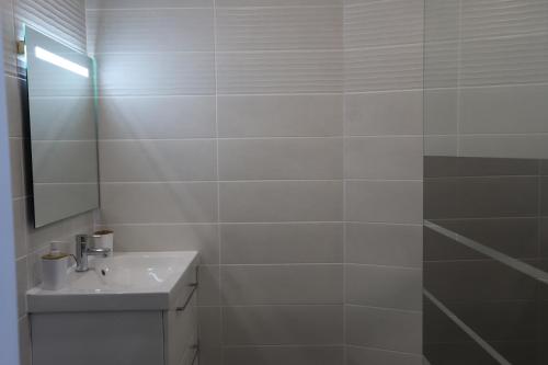 une salle de bain blanche avec un lavabo et un miroir dans l'établissement Appartement neuf climatisé, à Aramits
