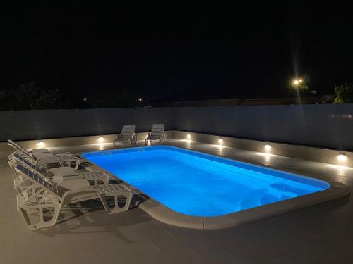 einen Pool in der Nacht mit Stühlen und einem Tisch in der Unterkunft Apartments Ukic - with large outdoor pool in Kaštela