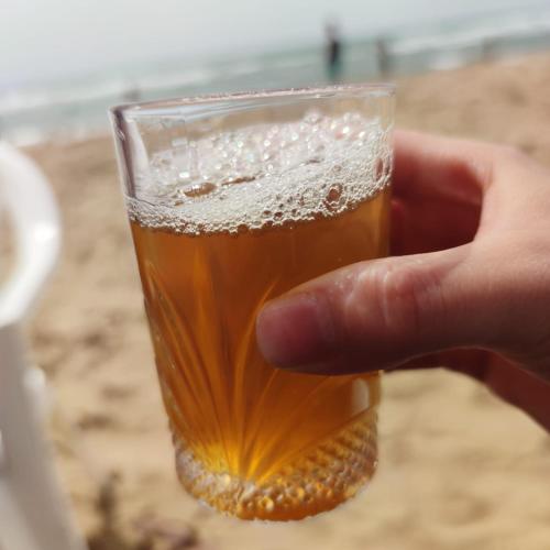 Eine Hand hält ein Glas Bier am Strand in der Unterkunft B&B restaurant OCÉAN in Briech