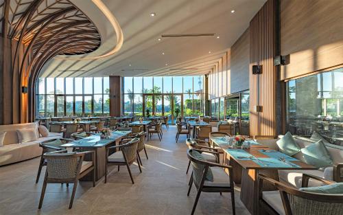 a restaurant with tables and chairs and windows at Bellerive Hoi An Resort and Spa in Hoi An