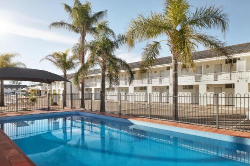 a swimming pool with palm trees in front of a building at ibis Styles Tamworth in Tamworth