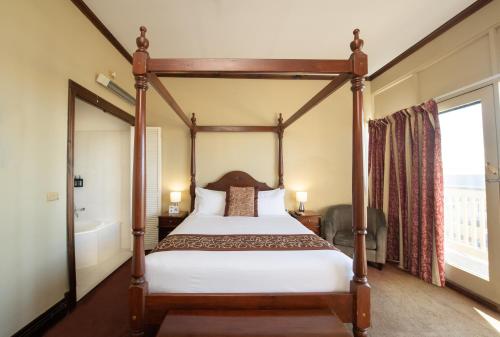 a bedroom with a four poster bed and a tub at Anchorage Seafront Hotel in Victor Harbor