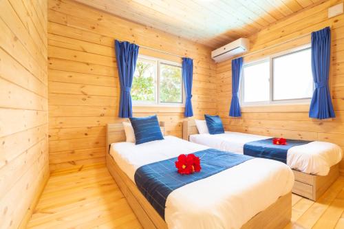2 łóżka w pokoju z drewnianymi ścianami i niebieskimi zasłonami w obiekcie レジーナ石垣　ログテリアⅠ w mieście Hirakubo