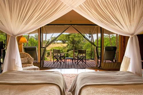 a bedroom with two beds and a porch with a deck at Elewana Sand River Mara in Talek