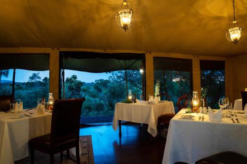 a dining room with tables and chairs and windows at Elewana Sand River Mara in Talek