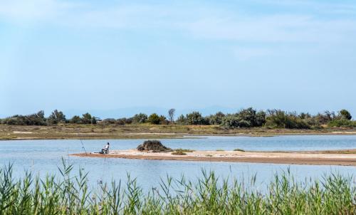 une personne pêchant sur une île dans l'eau dans l'établissement Maisonеtte Arcadia - vue sur l'étang, à Gruissan