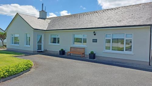 a white house with a bench in front of it at Southland Holiday Home by Trident Holiday Homes in Miltown Malbay