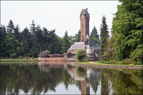 a large building with a clock tower next to a lake at Comfortabel tot rust komen in het Veluwse bos in Otterlo
