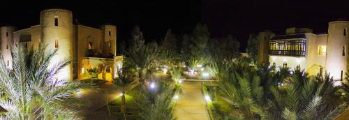 a night view of a building with palm trees and lights at Palais Du Desert Hotel & Spa in Erfoud