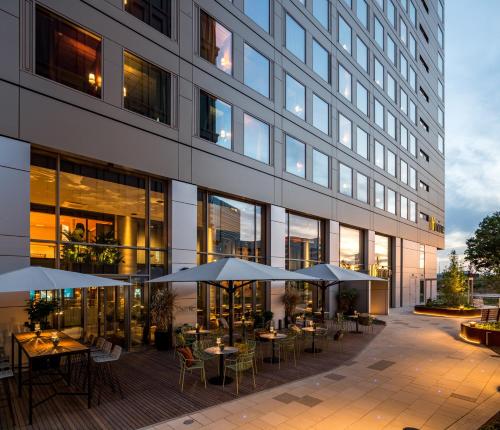 an outdoor patio with tables and umbrellas in front of a building at b'mine Hotel Frankfurt Airport in Frankfurt/Main
