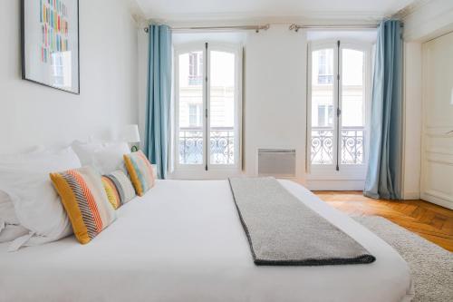 un grand lit blanc dans une pièce avec des fenêtres dans l'établissement Appartements Bergère, à Paris