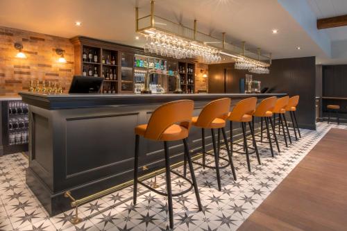 a bar with a row of orange bar stools at Horwood House Hotel in Milton Keynes