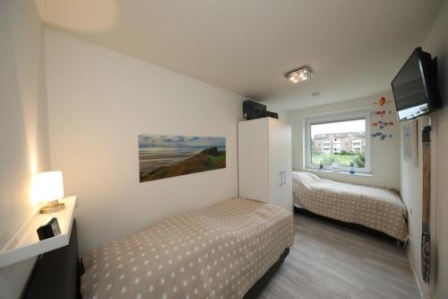 een slaapkamer met 2 bedden, een tv en een raam bij Quartier Hohe Geest 15 - Nordseebrise - a69852 in Cuxhaven