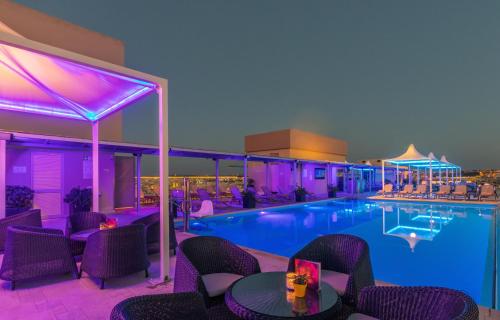 uma piscina do hotel com iluminação roxa e mesas e cadeiras em AX The Palace em Sliema