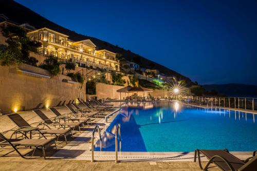 a swimming pool with chairs and a hotel at night at Kefalonia Bay Palace in Kefallonia