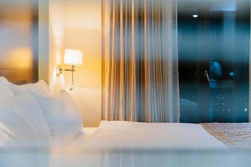 a bedroom with a bed with white sheets and a lamp at Hotel Dukagjini in Peje