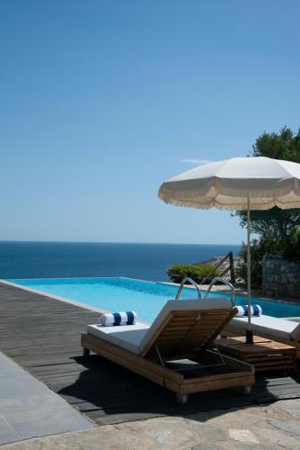 two lounge chairs and an umbrella next to a swimming pool at Villa Aiolos: above the sea, within Agios Nikolaos in Agios Nikolaos