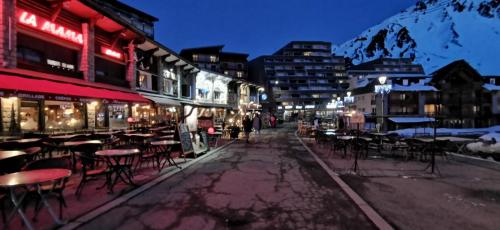 a street with tables and chairs in a city at night at Appartement T2 4 personnes, pied des pistes, parking privé, piscine in La Mongie