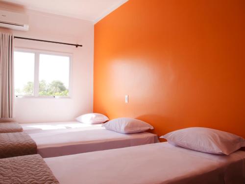 2 Betten in einem Zimmer mit orangefarbener Wand in der Unterkunft sempreHotel in Três Lagoas