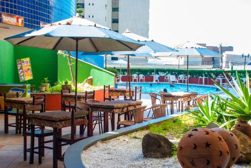 福塔莱萨Apartamento Praia de Iracema的一家设有桌椅、遮阳伞和游泳池的户外餐厅