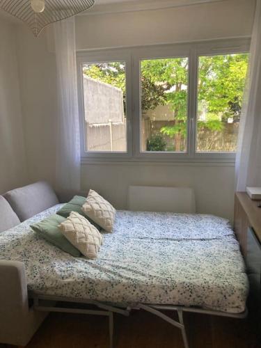 - une chambre avec un lit avec des oreillers et 2 fenêtres dans l'établissement Studio 5 min du centre-ville, à La Rochelle