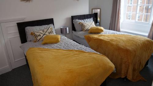 1 dormitorio con 2 camas y mantas amarillas en MK Shortstay Deluxe en Milton Keynes