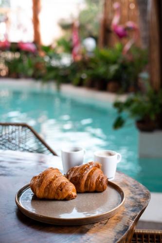 two croissants and coffee cups on a table next to a pool at Xkeban Tulum Adults Only in Tulum