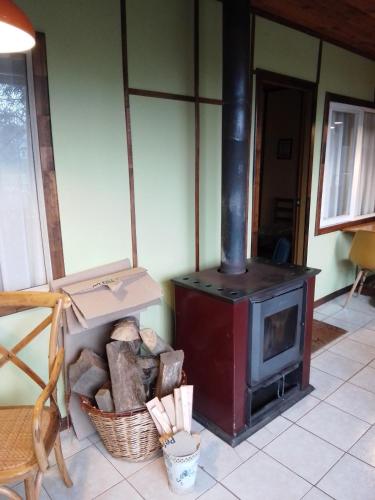 a wood stove in a room with a basket of logs at Cabaña la Solar. in Frutillar