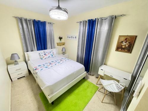 Un pequeño dormitorio con una cama blanca y cortinas azules en A-3 apartamentos al pie de la montaña con piscina, en Jarabacoa