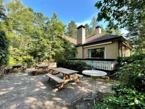 una mesa de picnic y bancos frente a una casa en Cosy villa in the middle of the woods in Doornspijk, en Doornspijk