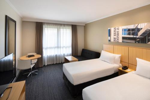 a hotel room with two beds and a television at Mercure Sydney Macquarie Park in Sydney