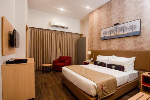 a hotel room with a bed and a red chair at Mastiff Hotel Ankleshwar in Ankleshwar