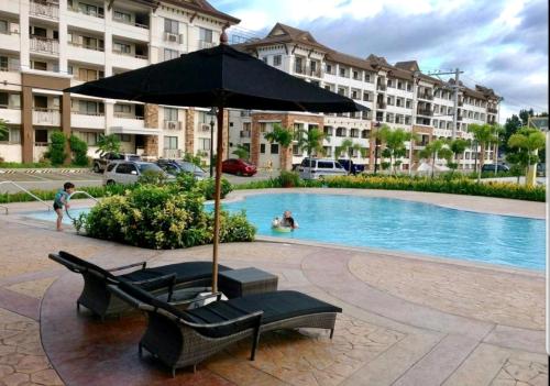 a pool with two chairs and an umbrella next to a building at Ri's One Oasis w Free Pool back of SM City Mall in Davao City