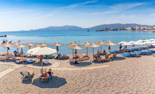 a beach with umbrellas and people sitting on the sand at New Loft by Ossiano Pool Villas, Heating Pool,2 min drive to Haraki Beach & 10 to Lindos in Haraki