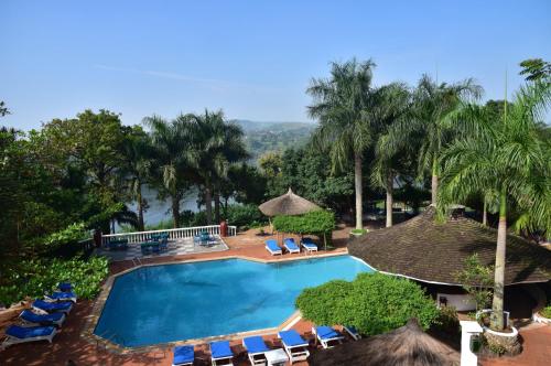 einen Pool mit Stühlen, Sonnenschirmen und Palmen in der Unterkunft Jinja Nile Resort in Jinja
