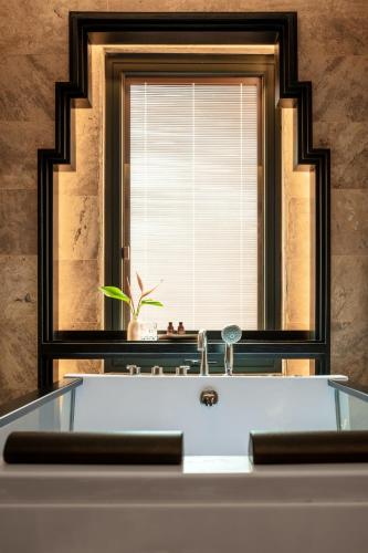 a bathtub in front of a window with a mirror at Ravatel Style Hotel Bac Giang in Bắc Giang