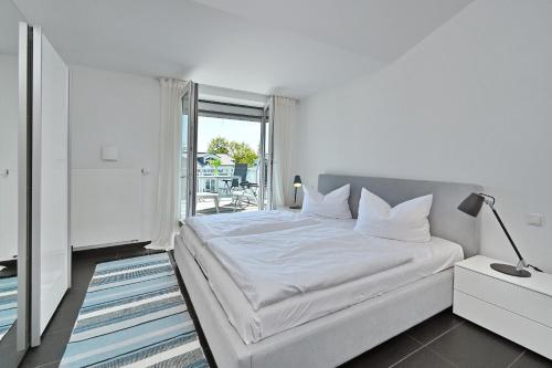 a white bedroom with a bed and a balcony at Ferienwohnung Kala in Juliusruh