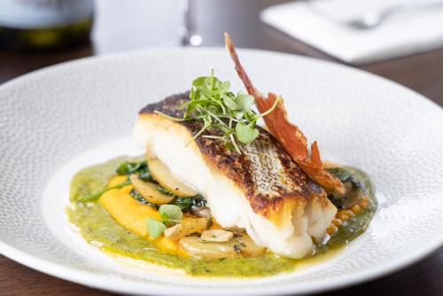 a white plate with a piece of fish and vegetables at The Ship in Parkgate