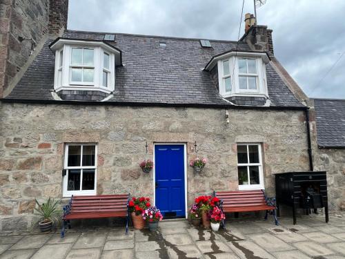 a stone house with a blue door and two benches at Unique 2 Bedroom Cottage in Fittie (Footdee) in Aberdeen