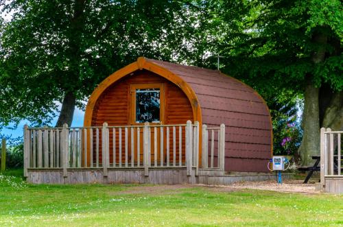 a small cabin with a fence in front of a tree at Drumshademuir Caravan & Camping Park in Glamis